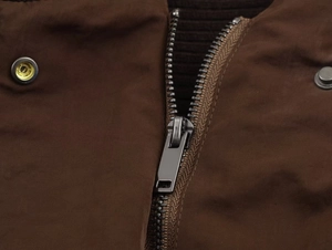 Close-up of high-quality metal zipper and textured fabric on dark brown jacket