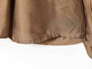 Close-up of the smooth hem and stitching on a glossy bronze silk-like fashion blouse