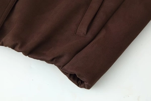 Detailed close-up of dark brown suede jacket featuring elastic hem and side pocket stitching