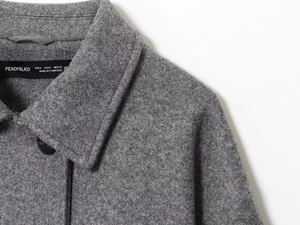 Detail of grey wool-texture coat lapel with dark button and premium woven fabric