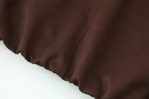 Detail of dark brown jacket showing precise stitching and elasticated hem texture
