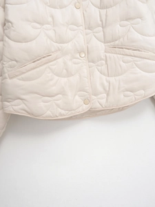 Detail view of beige quilted jacket featuring cute bow-shaped stitching and snap buttons