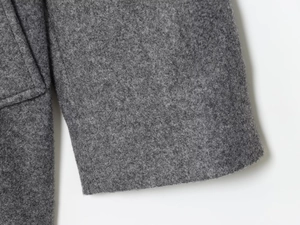 Detail shot of grey wool-blend coat showing textured fabric and stitching on pocket