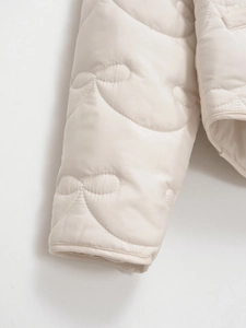 Close-up of cream quilted jacket sleeve with elegant bow patterns and smooth stitching