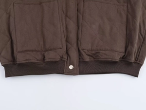 Détail d'une veste bomber matelassée marron foncé avec grandes poches et ourlet côtelé