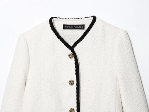 Detailed macro view of white tweed jacket featuring black woven trim and gold buttons