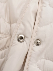 Close-up of silver metal snap buttons and circular quilting on cream puffer coat