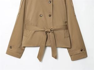 Detailed close-up of khaki trench coat featuring double-breasted buttons and tied bow belt