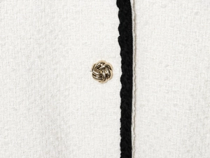 Macro shot of pearl white tweed fabric with black trim and gold knot button detail