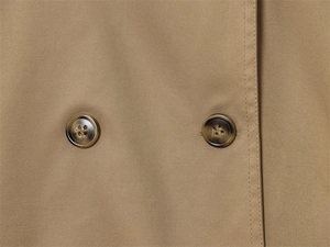 Detail of khaki trench coat featuring tortoise shell buttons and fine twill fabric texture