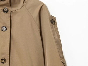 Close-up of tan trench coat detail showing raglan sleeves and textured buttons