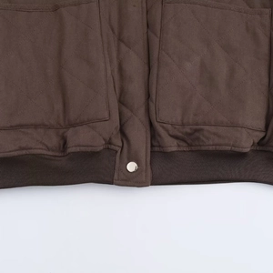 Gros plan d'une veste matelassée marron foncé avec coutures en losange et bouton argenté
