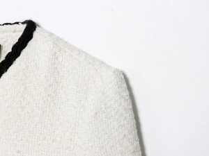 Detail of white tweed jacket shoulder featuring black woven trim and textured fabric
