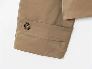 Detailed close-up of khaki trench coat cuff featuring a tortoiseshell button and neat stitching