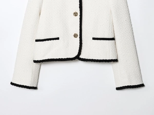 Close-up of white tweed jacket featuring black woven trim and gold twisted metal buttons