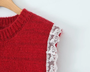 Detail of red knit vest with white floral lace trim on shoulder and ribbed crew neck