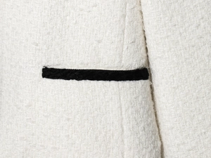 Detailed close-up of cream tweed fabric texture with a contrasting black woven trim