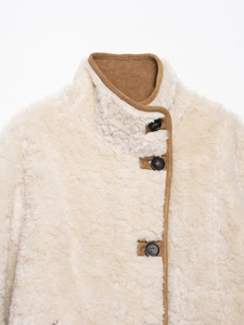 Detail der cremefarbenen Teddyjacke mit Stehkragen, braunem Wildlederbesatz und Knöpfen