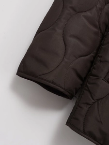 Close-up of wave-quilted dark brown jacket showing satin finish fabric and stitching
