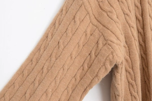 Detail view of the intricate cable-knit pattern and shoulder stitching on a camel sweater