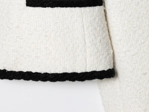 Close-up of beige tweed jacket fabric texture with black woven piping details