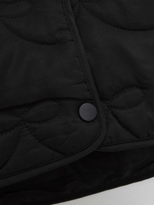 Detail of black quilted jacket featuring curved patterns and matte snap button