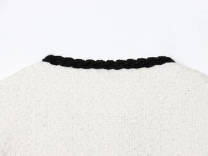 Close-up of white tweed jacket neckline with black braided trim and woven texture