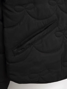 Detail of black quilted jacket showing elegant bow stitching patterns and pocket design
