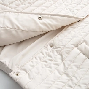 Detail of beige quilted vest featuring silver metal snap buttons and fine stitching