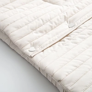 Detail of cream quilted jacket featuring unique heart-shaped buttons and neat stitching