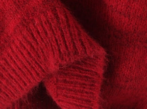 Macro shot of red knit sweater detailing fuzzy wool blend texture and ribbed cuffs