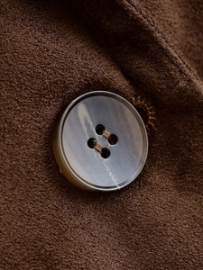 Detailed close-up of marble texture four-hole button on brown suede blazer fabric
