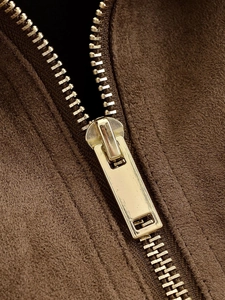Close-up of golden metal zipper on brown suede jacket showing detailed texture and finish