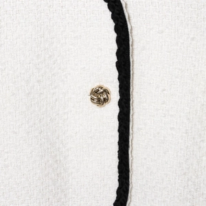 Close-up of white tweed jacket with black braided trim and a decorative gold metal button