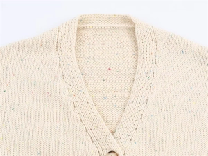 Detail of V-neck confetti yarn knit cardigan with amber textured button on white surface