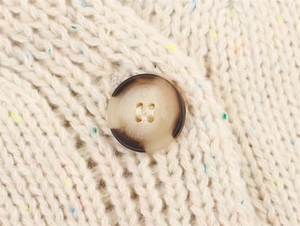 Close-up of beige chunky knit sweater texture with colorful flecks and brown resin button