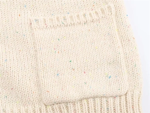 Close-up of beige speckled knit sweater featuring a square pocket and ribbed texture
