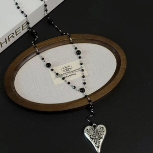 Silver hollow heart cross pendant with black beaded necklace on a wooden tray