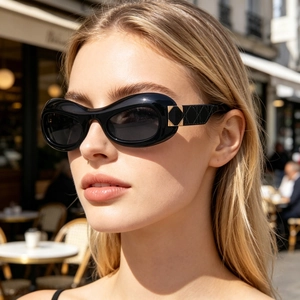 Close-up of black oval sunglasses with golden hardware and quilted pattern on the temples