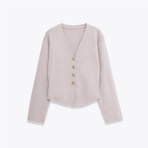 Detail of V-neck knit cardigan with four gold-tone metal buttons on lavender fabric