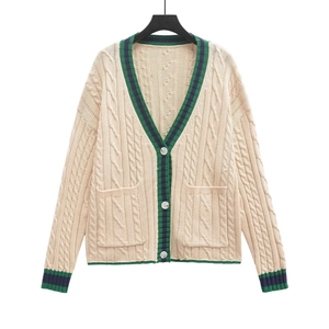 Macro view showing cable knit patterns and navy green striped ribbon trim on beige cardigan
