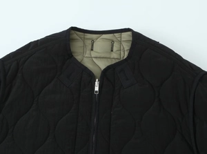 Detailed view of black onion-quilted jacket featuring metal zipper and olive green lining