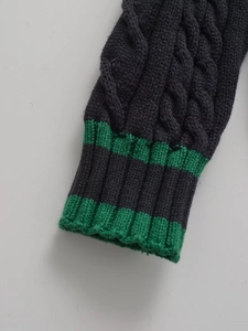 Detail of cable knit texture on sleeve with green stripes and ribbed cuff design