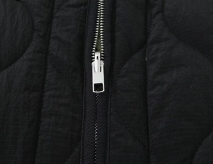 Close-up of silver metal zipper and circular quilted texture on black puffer jacket
