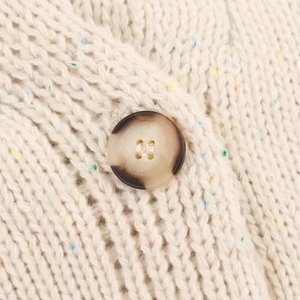 Close-up of loose-fit white knit sweater with colorful speckled yarn and marbled button