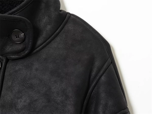 Détail d'une veste en cuir noir montrant la texture mate, la doublure et le bouton