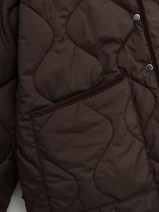 Close-up of brown quilted jacket with corduroy trim pockets and metal snap buttons