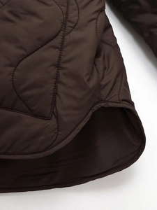 Detail of dark brown quilted jacket showing curved hemline and fine stitching texture