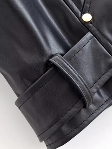 Détail d'une veste en similicuir noir avec texture litchi et bouton doré en métal