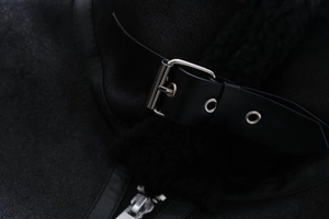 Detailansicht der schwarzen Lammfelljacke mit Lederriemen und silbernen Metallschnallen